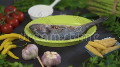 新鲜的生的多拉达鱼，放在绿色的盘子里，黑桌上放着一套蔬菜
